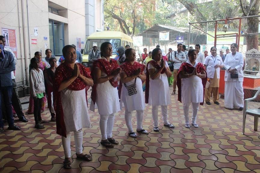 a group of five people dressed alike standing outside with their hands pressed together in front of their chests, people stand around them looking toward them