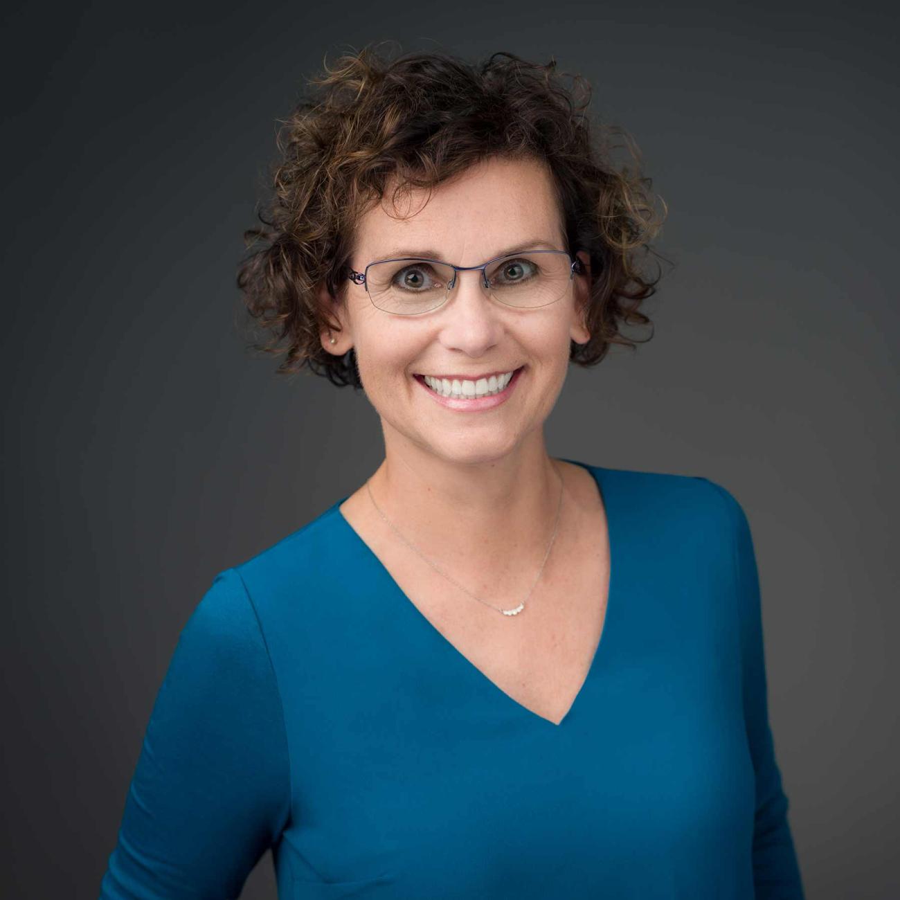 Image of Dr. Brookie Best, PharmD. She is smiling and has short brown curly hair, glasses, and is wearing a blue shirt.
